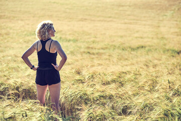 A woman in a black tank top and shorts stands in a field of tall grass