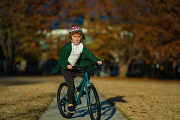 Naklejka premium Cute kid boy riding a bike in the autumn park. Little kid boy in warm clothes in autumn park driving a bicycle. Active child cycling on sunny fall day in nature. Autumn leisure with kids.