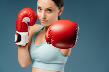 Close up of young sporty woman with red boxing gloves, doing punch looking at camera
