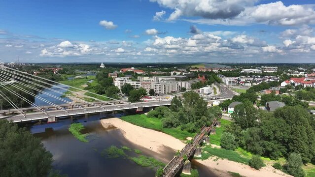 Flight from right to left next to the Emperor Otto Bridge in Magdeburg. Sunny weather, cloudy sky. Apartment blocks in the background, trees in the foreground. The bridge is a new building from 2024