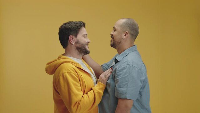 Authentic shot of young happy smiling married homosexual male gay couple on isolated yellow background studio, hugging and kissing.

