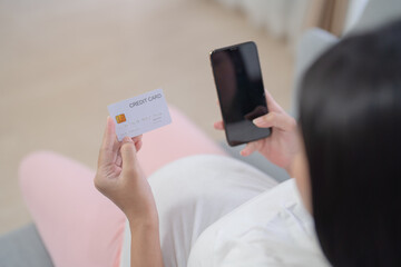 A portrait of happy Asian pregnant woman using a mobile phone device with credit card, shopping online in bedroom at home. Having a baby. Family people lifestyle. Mom love.