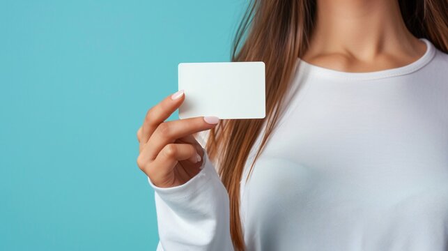 Front shot of a lovely smiling woman holding a white credit card, standing against blue background - Powered by Adobe