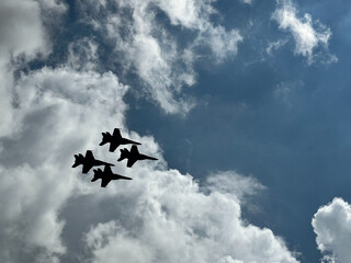 Four F-18 fighter jets flying in a diamond formation framed by white clouds and blue skies