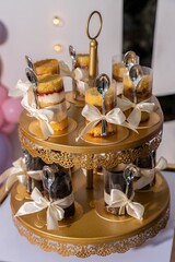 Display of layered dessert cups with spoons tied with ribbons on a gold tiered stand