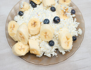 Cottage cheese with banana mixed in a plate on a blue background. breakfast with blueberries and cheese, sports nutrition with berries and cottage cheese