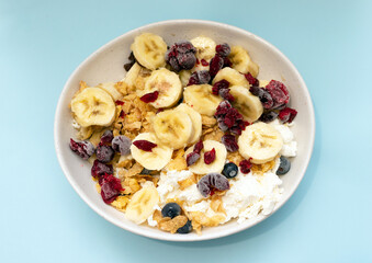 Bananas with blueberries, cottage cheese and raisins in a plate in the kitchen. Appetizing bananas with black berries and frozen cherries