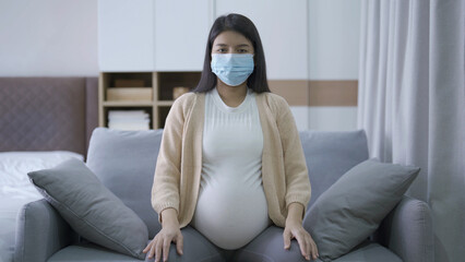 Depressed lonely Asian pregnant divorce woman with a mask for protecting covid-19 in bedroom at home. Having a baby. Family people lifestyle. Mom. quarantine