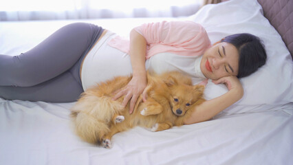 A portrait of happy Asian pregnant woman with domestic dog pet animal in bedroom at home. Having a baby. Family people lifestyle. Mom love.