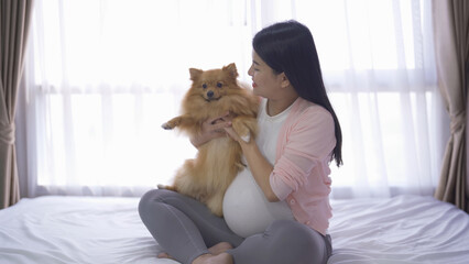 A portrait of happy Asian pregnant woman with domestic dog pet animal in bedroom at home. Having a baby. Family people lifestyle. Mom love.