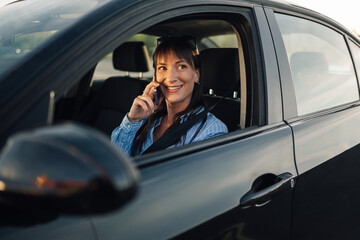 Portrait of smiling young woman sitting in car and talking on her phone