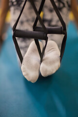 Person in grey sportswear exercising on yoga mat with suspension strap