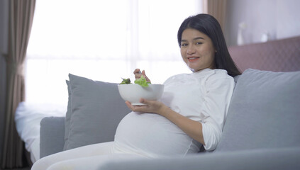 A portrait of happy Asian pregnant woman eating salad vegetable food for dieting in bedroom at home. Having a baby. Family people lifestyle. Mom love.