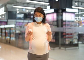 A portrait of happy Asian pregnant woman customer walking along supermarket, buying items on grocery products shelves with basket. Food shopping. Having a baby. Family people lifestyle. Mom.