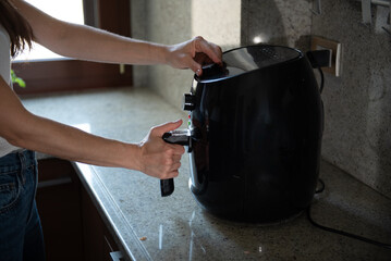 Woman is using a new black air fryer in a modern kitchen