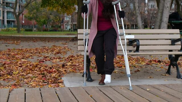 woman sitting on a bench in the park with a foot injury using crutches