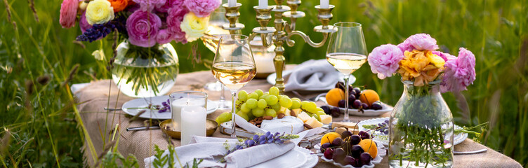 Surprise romantic date outdoors in a meadow. Elegant table with snacks and wine, chandelier with candles as decor. Private party celebration of special event for loving couple. Banner