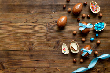 Chocolate Easter eggs in blue ribbon with sweets on brown wooden background