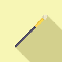 Makeup brush is laying on a light yellow background, casting a long shadow