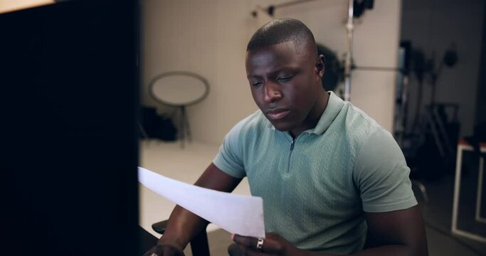 Black man, photographer and reading with documents for production, budget or expenses at studio. Young African, male person or producer checking paperwork for bills, finance or script at workplace