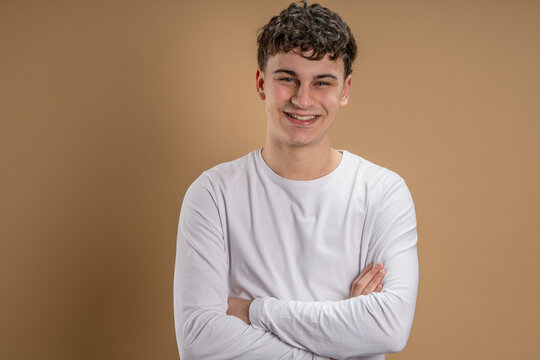 Portrait of one caucasian man 20 years old looking to the camera in front of almond color studio background smiling wearing casual shirt copy space