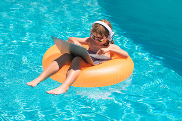 Summer travelling. Funny little businessman freelancer relaxing in the pool, using laptop computer in summer water. Child online working on tropical sea. Freelance work concept.