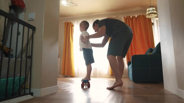 Father teaches his son to skateboard. Skate skater board family dream concept. A child is learning to skateboard indoors. Father teaches his son how to fun skateboard indoors happy childhood.