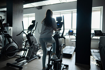 Young Female Athlete Exercising on Elliptical Trainer in a Gym, view from the back