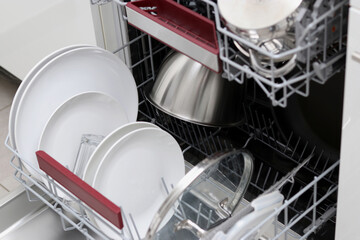 Close up of a full dishwasher with clean plates, lids, glassware in the kitchen