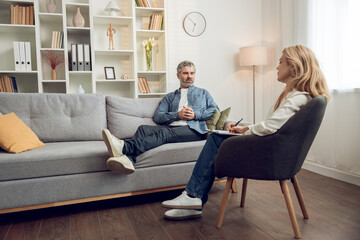 Man sitting on couch in counseling office and complaining about his troubles to female psychologist