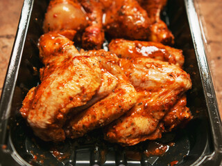 A tray of chicken wings and drumsticks is sitting on a counter. The product is covered in a sauce and are ready to be cooked. Asian style marinated poultry. Barbeque style food.