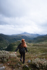 Fototapeta premium Eine Frau mit wehenden Haaren rennt kamera abgewand durch die Berge