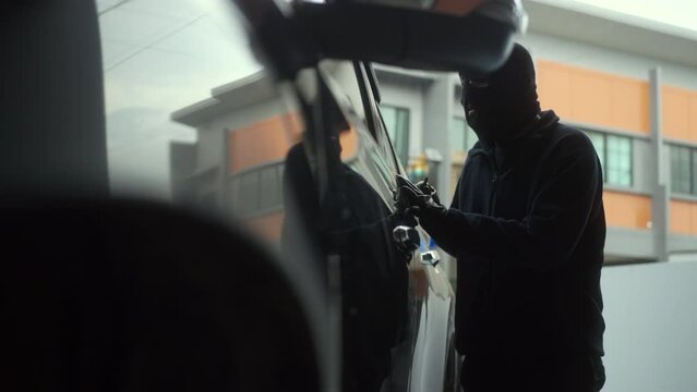 The creepy thief with wearing black mask sneaking around the car and try to break unlock the door's handle of vehicle, robber looking at the car to steal, car security system to prevent crimination.
