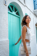 Young Woman in White Pants and Shirt by quamarine door and White Facade