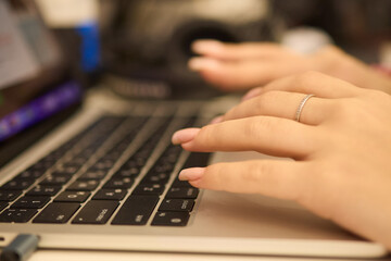A closeup showing hands typing on a laptop keyboard, with an engagement ring on the finger