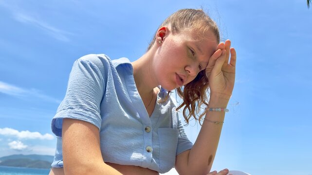 Young woman feeling bad, suffering from sunstroke at sea, beach at summer