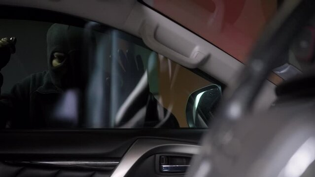Inside view of the creepy thief with wearing black mask looking inside the car and try to break unlock the door's handle of vehicle, car security system to prevent crimination.

