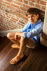 Portrait of a young boy sitting on stairs looking up at the camera with a curious expression	