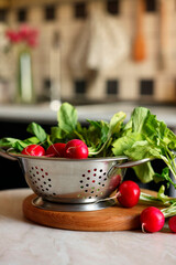 Metal colander with fresh radishes on white table