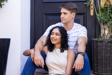 Diverse couple sitting together on steps, looking content