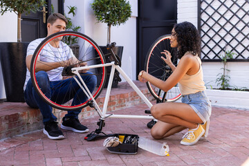 Diverse couple fixing bicycle together outdoors
