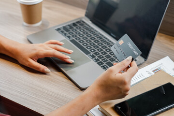 A woman is using a laptop to pay for something with a credit card. She is holding the card in her hand and she is focused on the transaction
