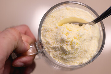 Whole milk powder in a glass cup that a man is holding.