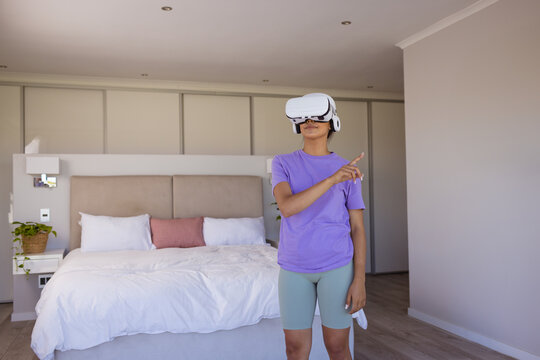 Happy biracial woman using virtual reality headset in modern bedroom, copy space