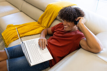 Happy biracial man relaxing on couch with laptop and headphones
