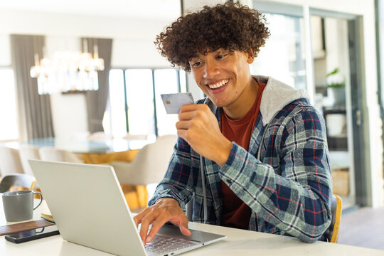 Happy biracial man holding credit card while using laptop, shopping online - Powered by Adobe