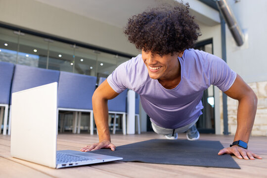 Biracial, Fit man exercising doing push-ups, focused on laptop screen, looking strong and fit