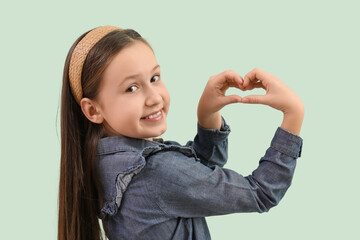 Cute little girl making heart with her hands on green background
