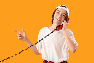 Cool teenage boy with phone receiver pointing at something on yellow background