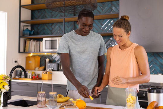 Happy, diverse couple prepping fruit in a modern kitchen for wellness and healthy living